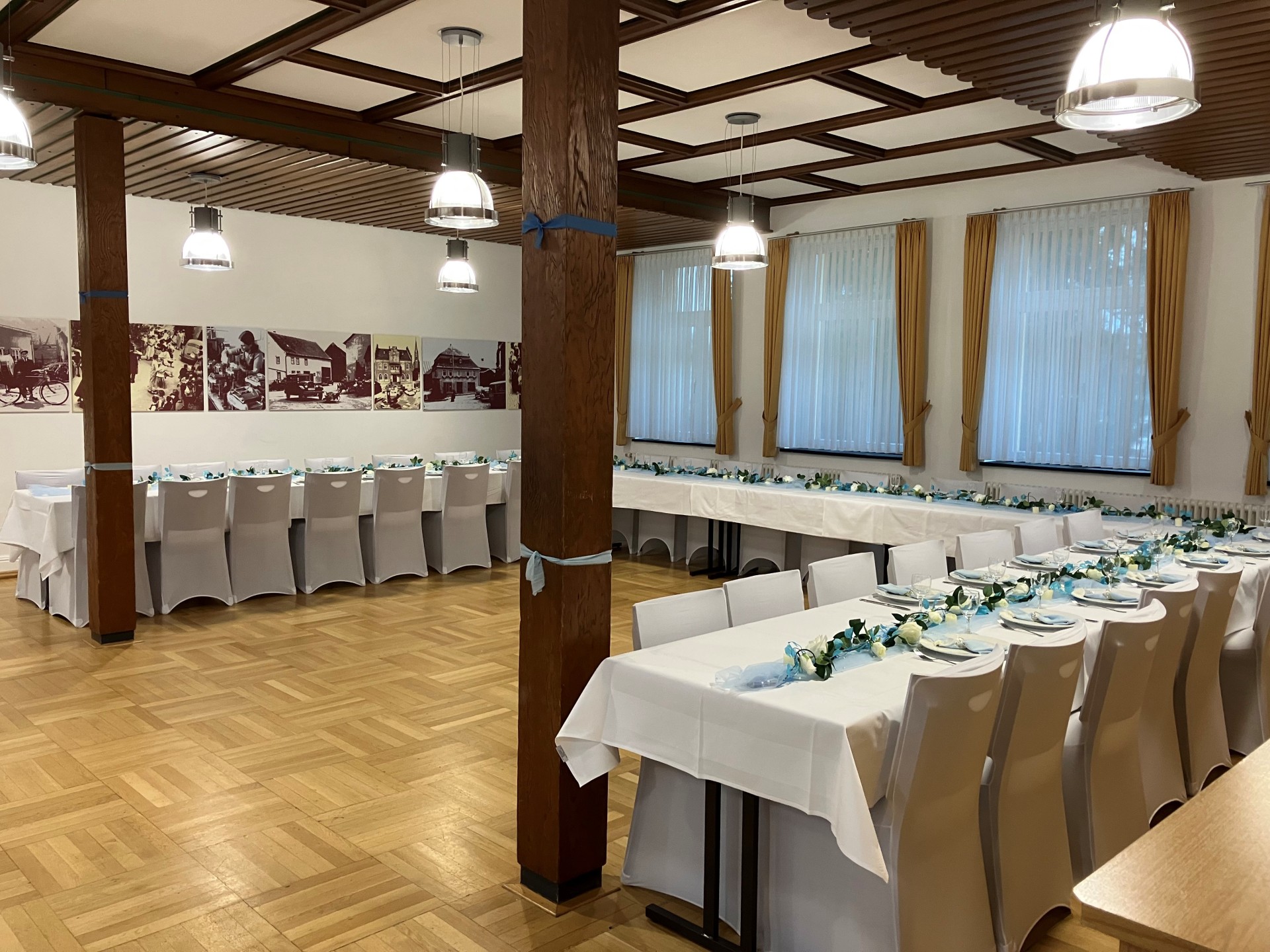 Alter Schulsaal in Rheinböllen mit gestellten Tischen und Deko. Zu sehen ist ein Holzfußboden und schwarz-weiß Aufnahmen an den Wänden