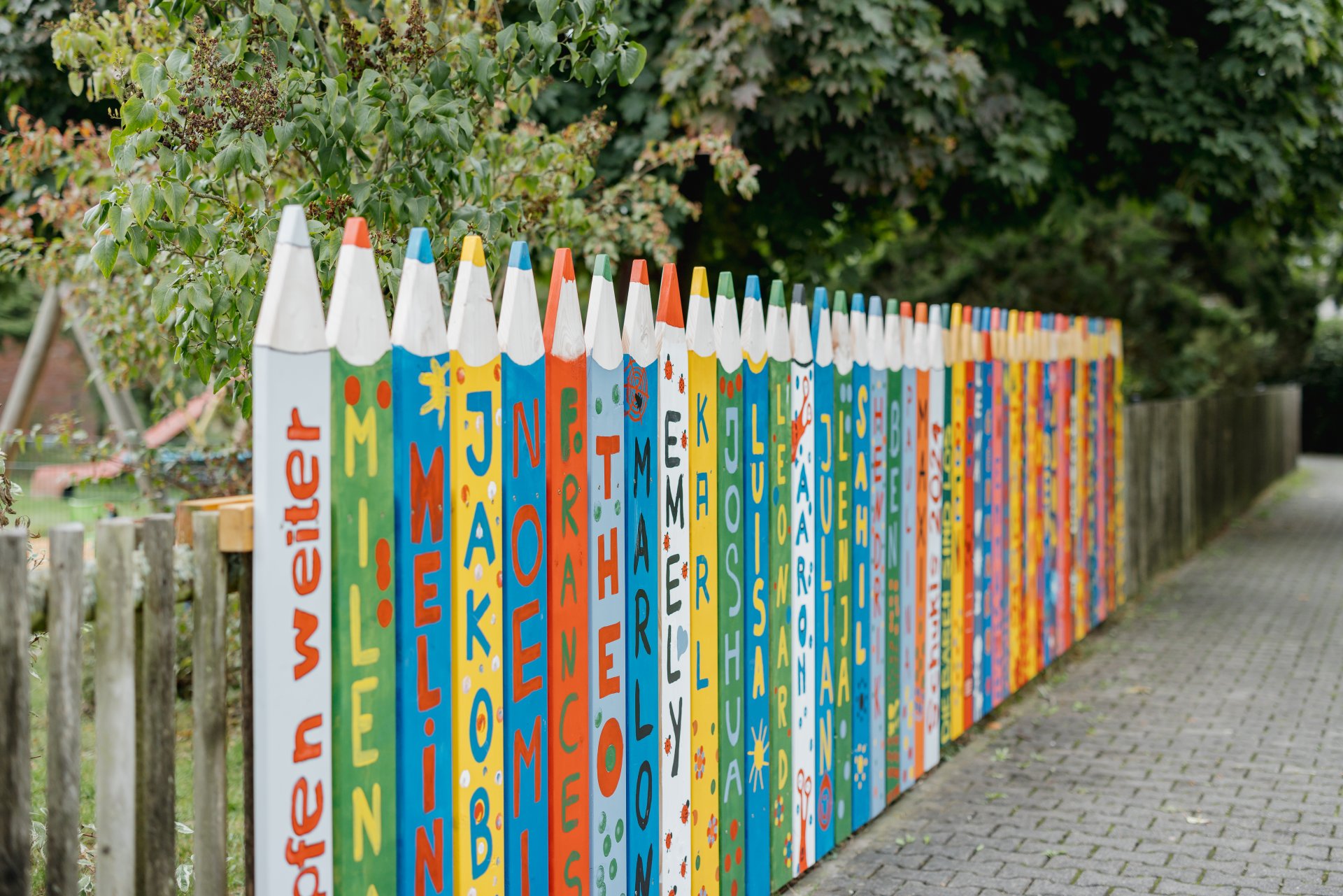 Außenanlage einer Kindertagesstätte mit bunt angemalten übergroßen Stiften am Zaun.